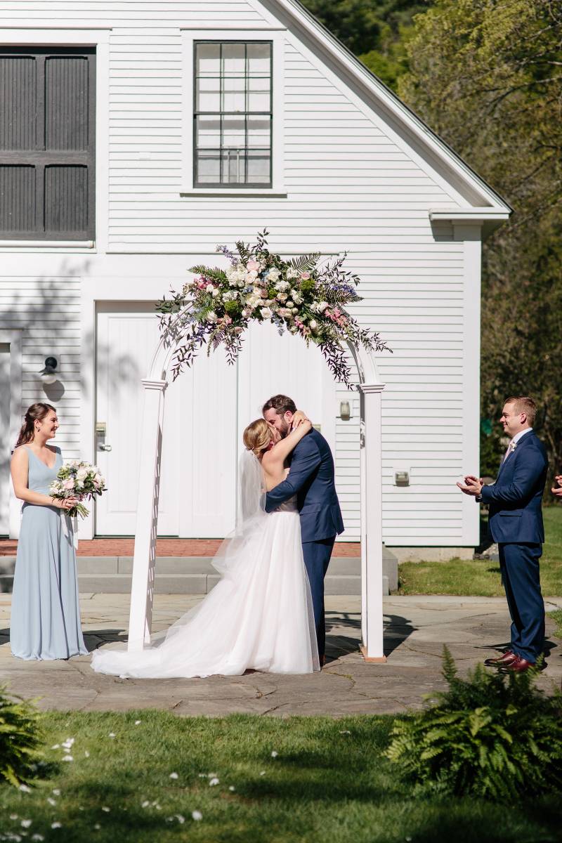 Couple kissing after ceremony under floral archway during spring wedding at the Woodstock Inn