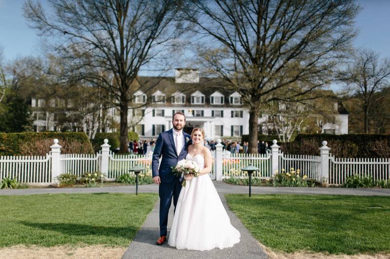 Bride and groom smiling in front of the Woodstock Inn in Vermont on spring wedding day