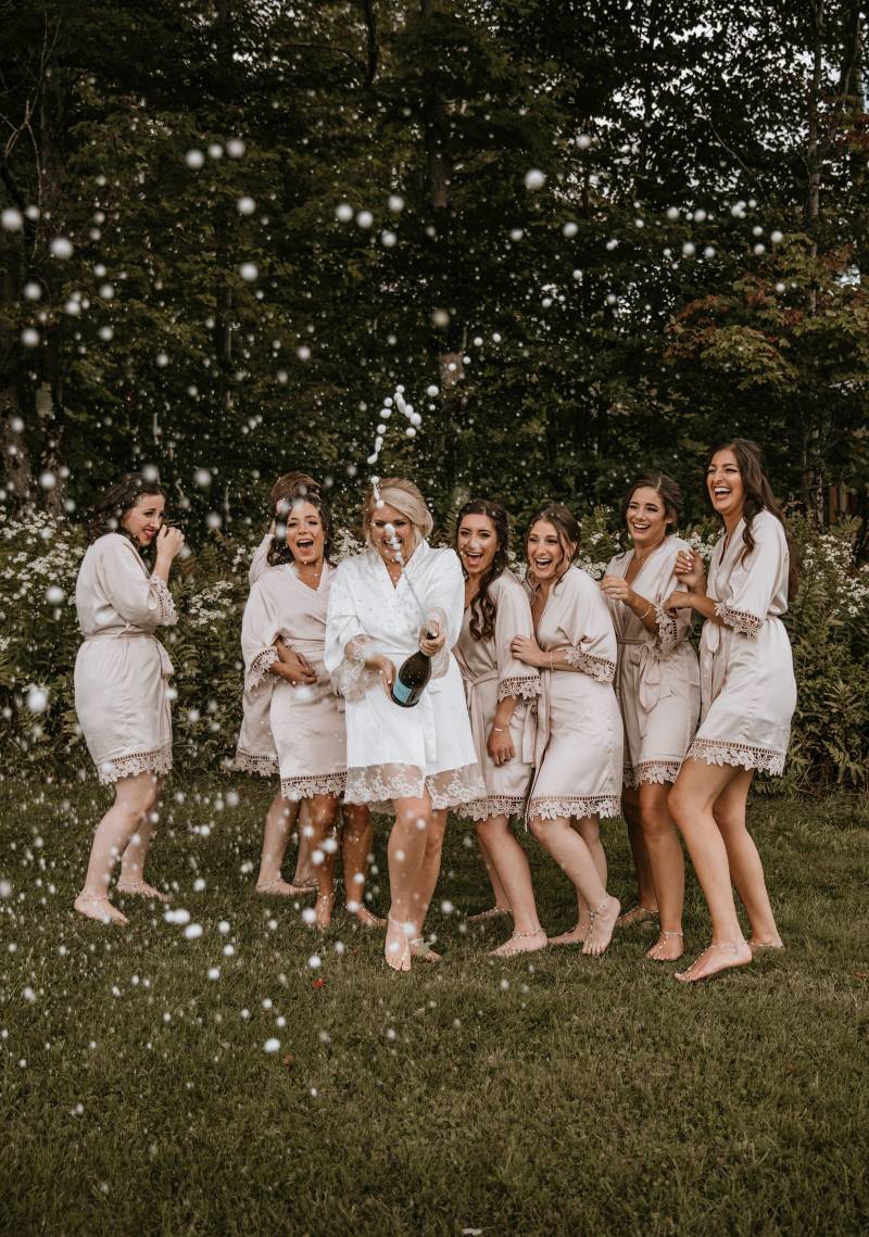 Brides popping champagne with bridesmaids in getting ready robes
