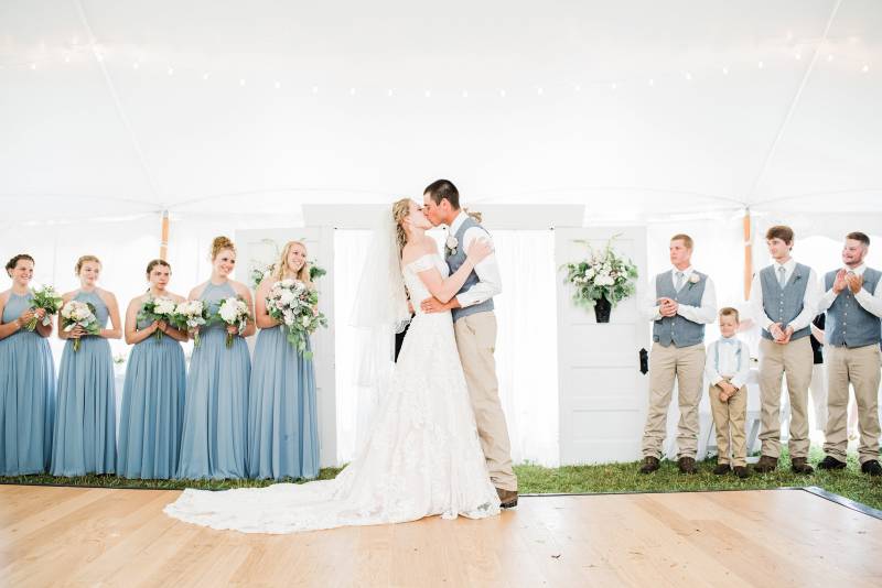 Couple kissing during summer tented ceremony with custom door backdrop