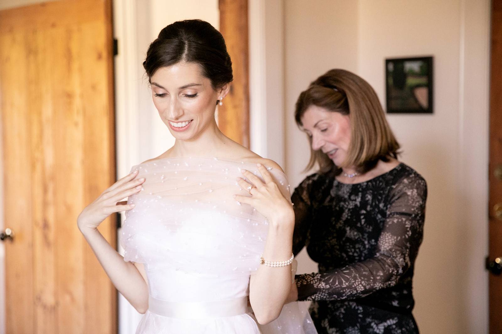 Bride's mom helping bride put on sheer shawl for fall outdoor wedding over strapless ballgown
