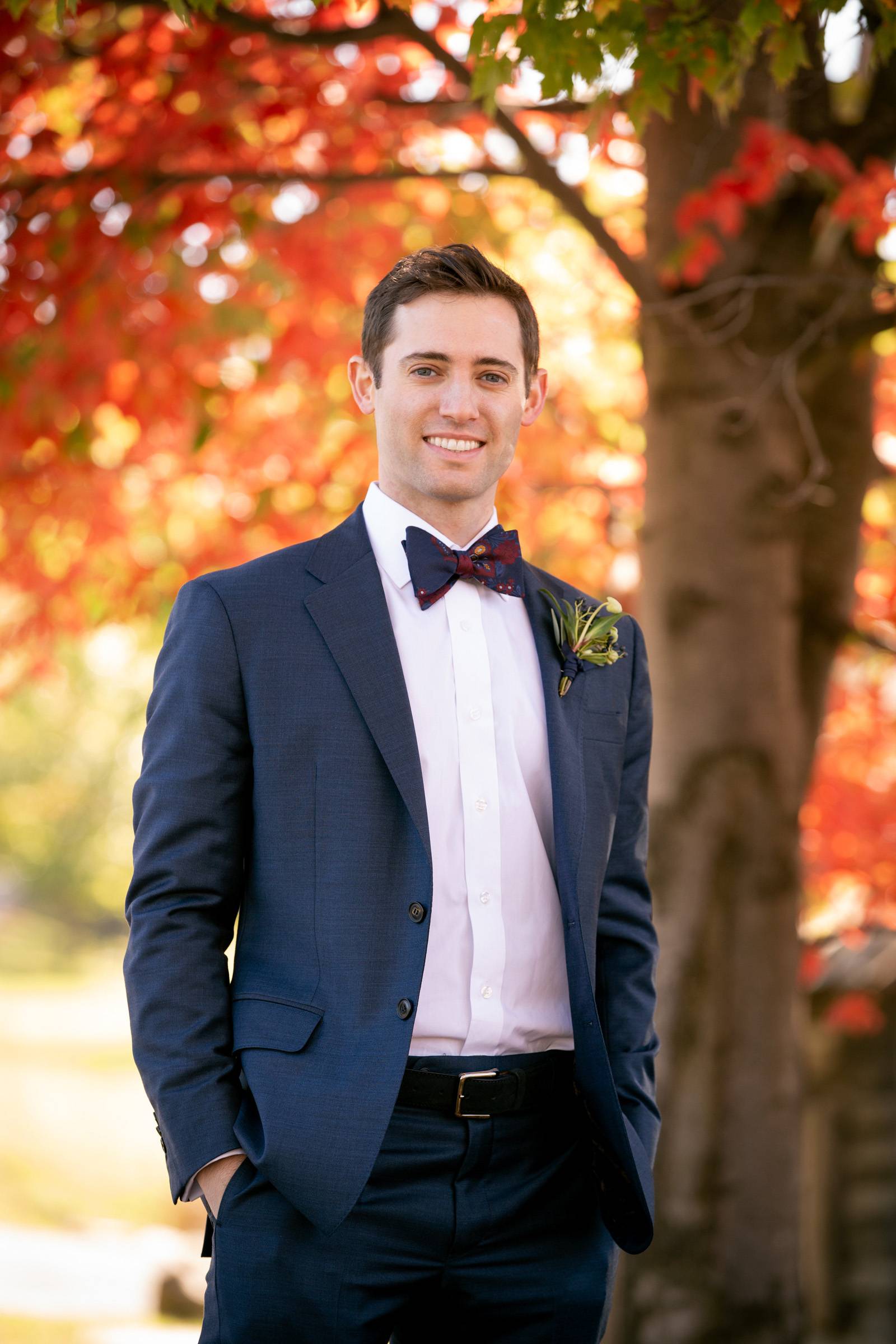 Groom in navy suit with navy and burgundy bowtie for fall wedding