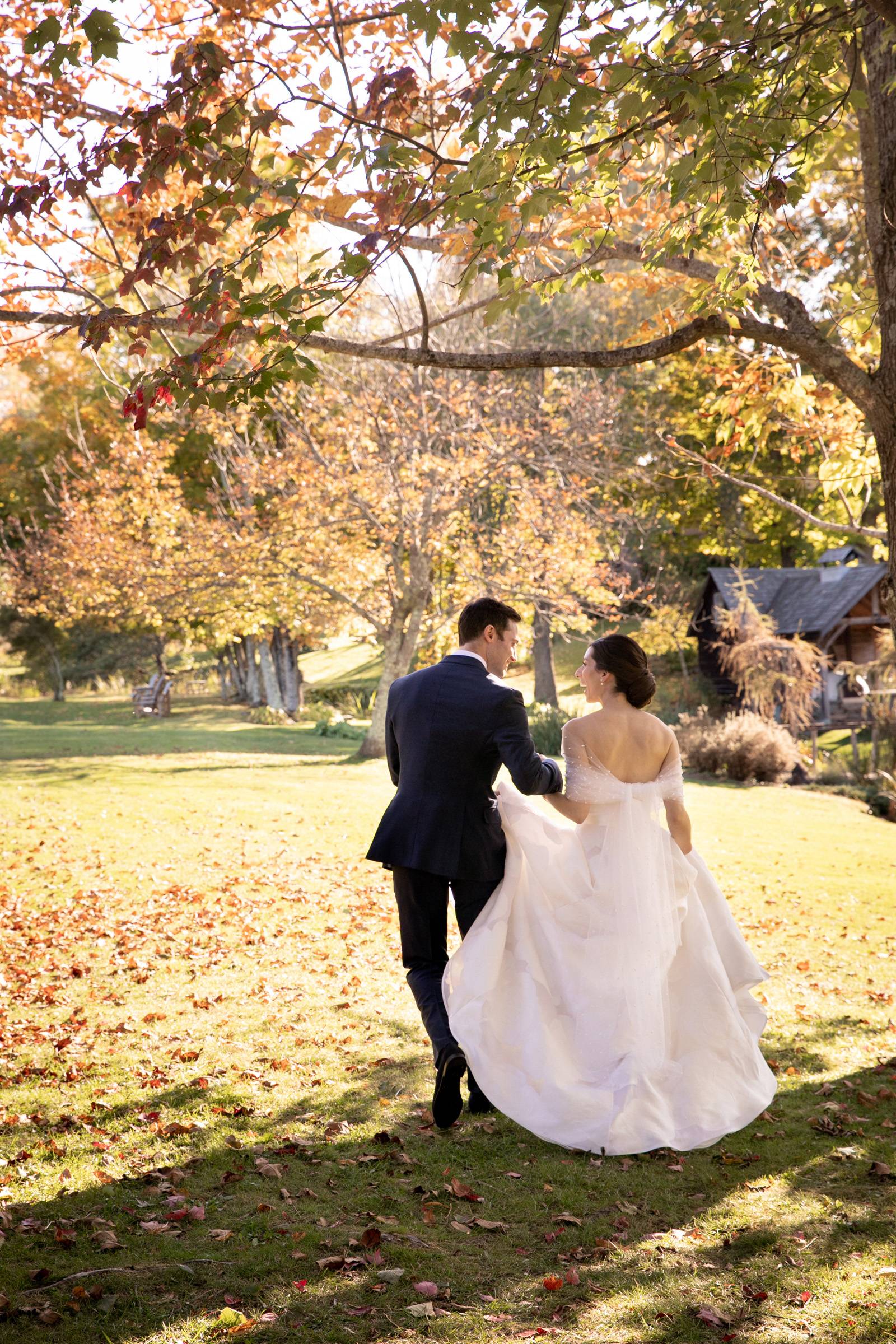 Bride and groom walking under tree after ceremony on fall wedding day in Vermont