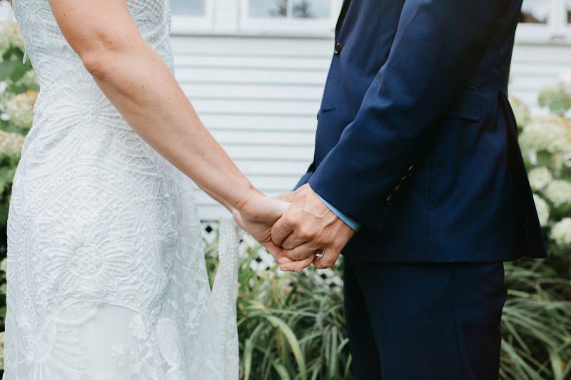 Close up of bride and groom holding hands, showcasing bride's lace dress